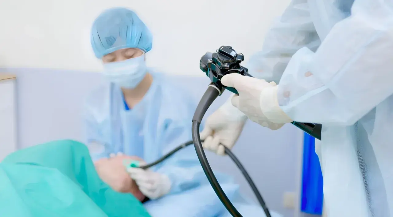 Lekarz w rękawiczkach i fartuchu przeprowadza gastroskopię, badanie pozwalające zajrzeć do żołądka.