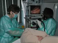 Lekarze w zielonych fartuchach obserwują obraz z wnętrza żołądka na monitorze, pokazując, jak wygląda gastroskopia.