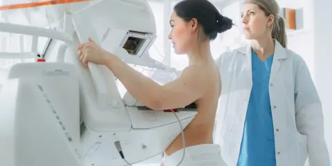 Kobieta podczas badania mammograficznego, które jest bezpieczne i kluczowe dla wczesnego wykrywania chorób. Lekarka nadzoruje proces.