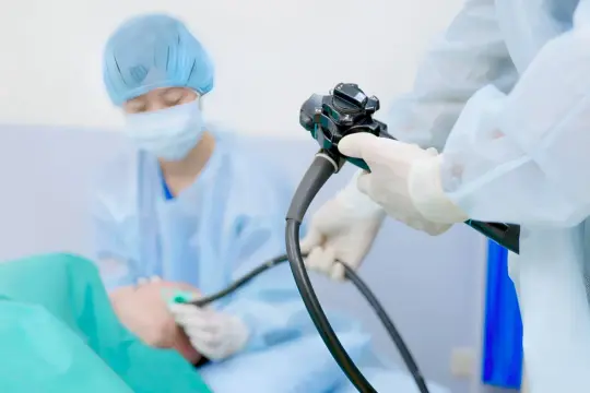 Lekarz w rękawiczkach i fartuchu przeprowadza gastroskopię, badanie pozwalające zajrzeć do żołądka.
